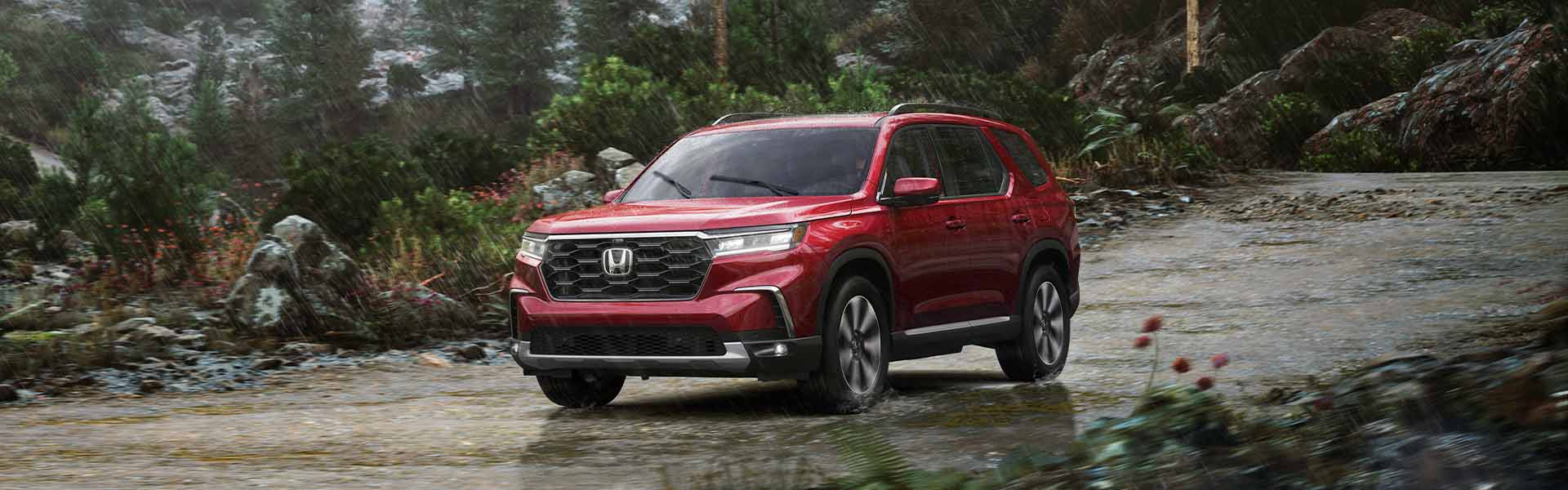 2026 Honda Pilot SUV driving on a wet forest road, red exterior.