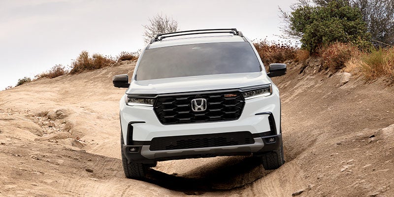 2026 Honda Pilot SUV driving on a dirt trail in a desert landscape, front view.