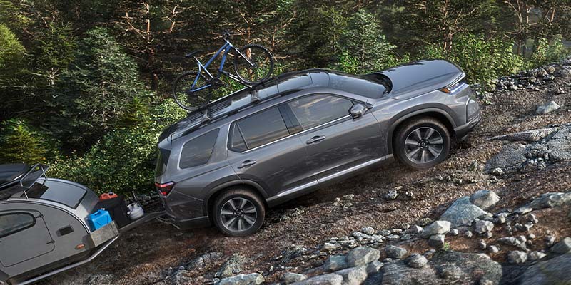 SUV parked on rocky forest slope with bicycles on roof rack.