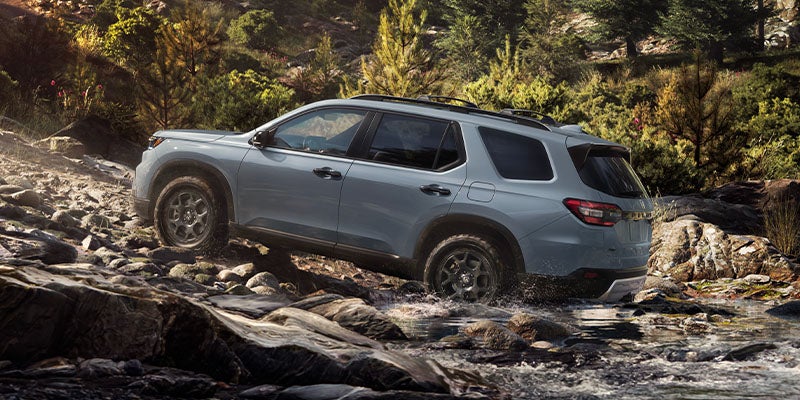 Honda Pilot SUV driving through rocky stream in a forest, side view.
