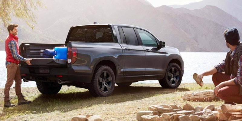 Honda Ridgeline pickup parked by lake with dog and mountains in background.