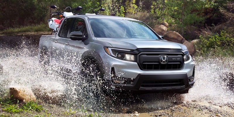 Front view of Honda Ridgeline pickup driving through water splash on off-road trail.