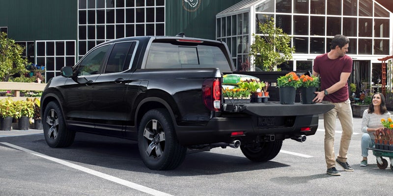 Black Honda Ridgeline pickup with tailgate open, loaded with potted plants being loaded in suburban driveway.